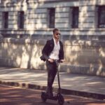 Man in a suit riding an electric scooter on a city street, showcasing modern urban transportation.