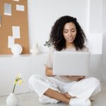 Young woman with curly hair working on her laptop in a cozy home setting, exuding confidence and focus.