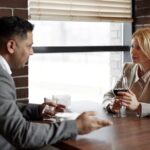 Two business professionals discussing ideas over a glass of wine in a modern café setting.