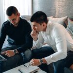 Two men discussing market trends using a tablet in an office setting.