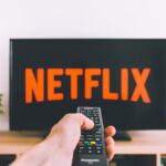 A hand holding a TV remote in front of a screen with Netflix, perfect for streaming and movie night themes.