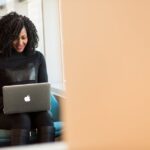 African American woman happily working on a laptop in a modern office setting.
