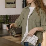 A woman with curly hair cleans a kitchen counter using a spray bottle and cloth.