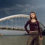 Stylish female model posing by Humber Bay Arch Bridge in Toronto, outdoors on a sunny day.