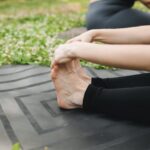 Close-up of a woman stretching on a yoga mat outdoors, promoting fitness and wellness.