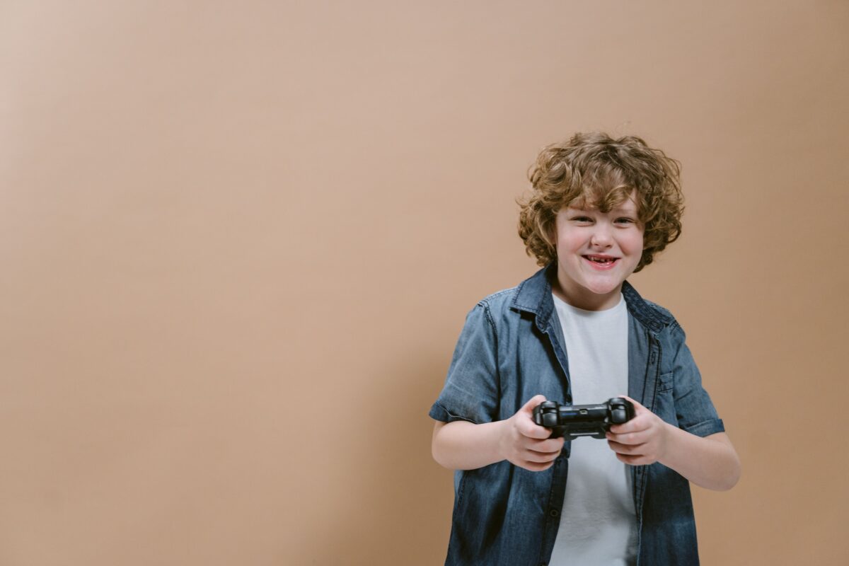 A happy child holding a game controller, enjoying video gaming indoors against a plain background.