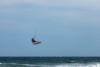 Kitesurfer performing midair tricks against a vast ocean backdrop, showcasing skill and adventure.