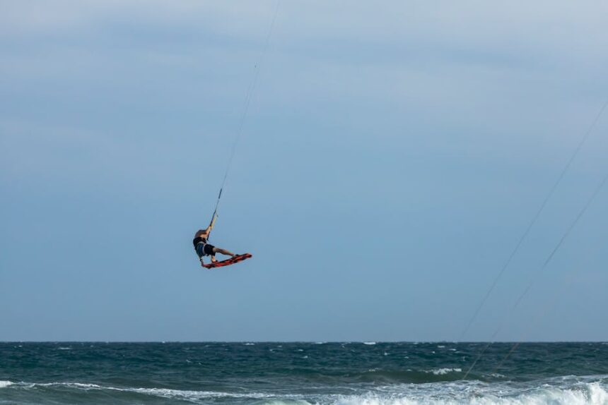 Kitesurfer performing midair tricks against a vast ocean backdrop, showcasing skill and adventure.