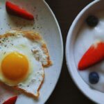 a white plate topped with a fried egg next to a bowl of fruit