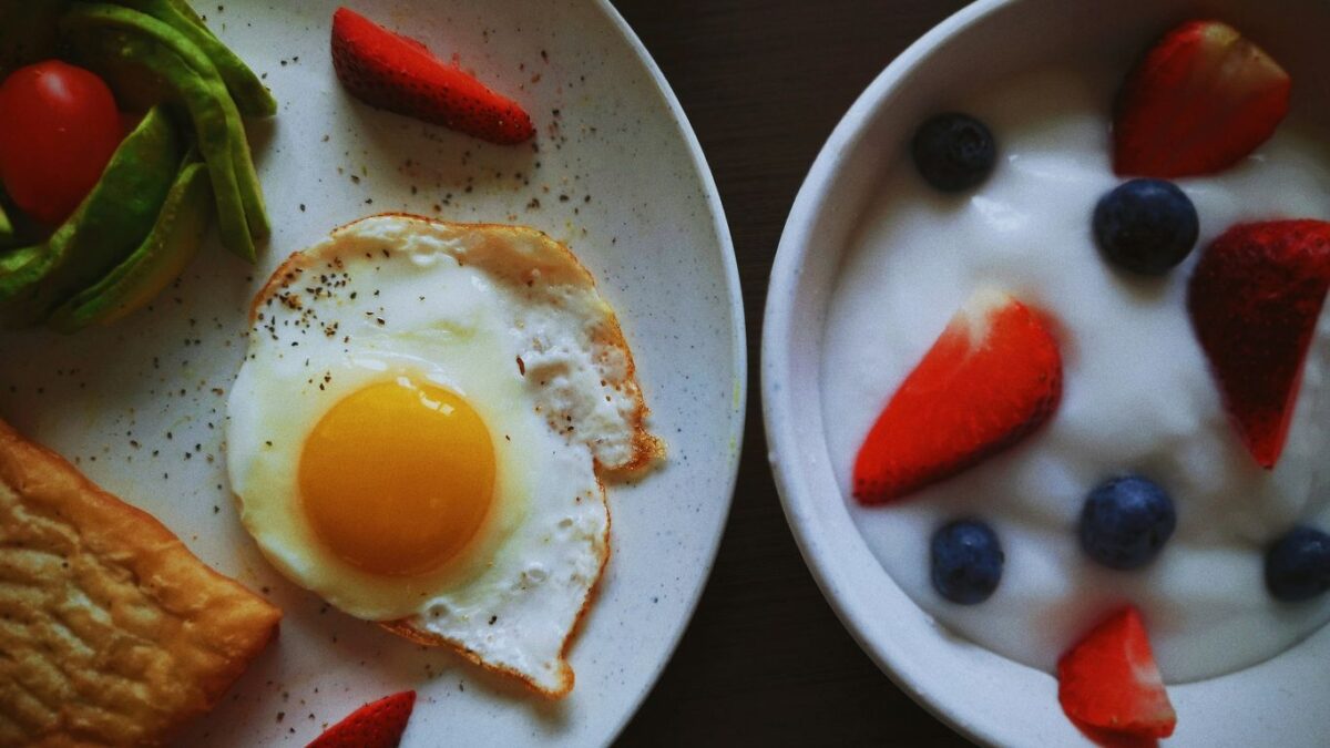 a white plate topped with a fried egg next to a bowl of fruit