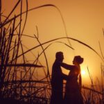 silhouette of man and woman standing on grass field during sunset