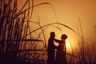 silhouette of man and woman standing on grass field during sunset
