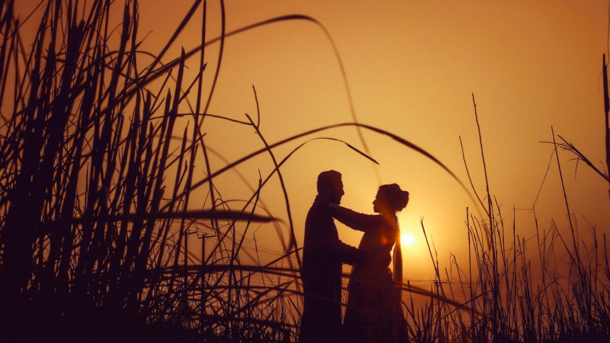 silhouette of man and woman standing on grass field during sunset